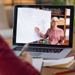 Laptop screen with female teacher pointing at whiteboard