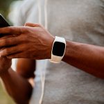 male athlete wearing fitness tracker on left wrist using smartphone with both hands