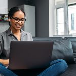 Woman at home sitting on couch working on laptop