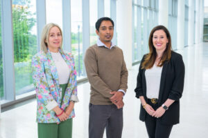 Three Incyte professionals pose by large picture windows overlooking Wilmington