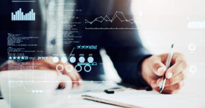 man writing with a pen, cup of coffee in the foreground and technical data and graphs superimposed on the image.